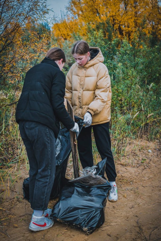 girls-collecting-trash-in-forest-9620519 Two teenagers collect trash in a forest during autumn, promoting environmental awareness.